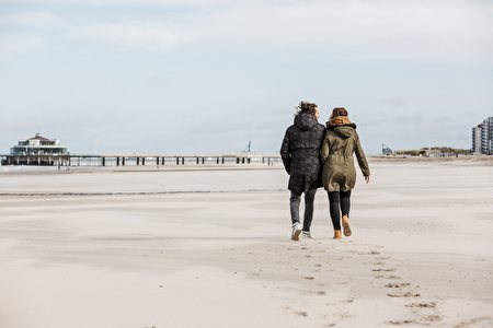 Koppel en tenue d'hiver marche sur la plage en direction de la jetée.